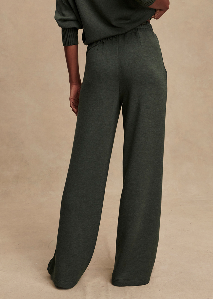 Woman wearing dark green wide leg pants against a tan background