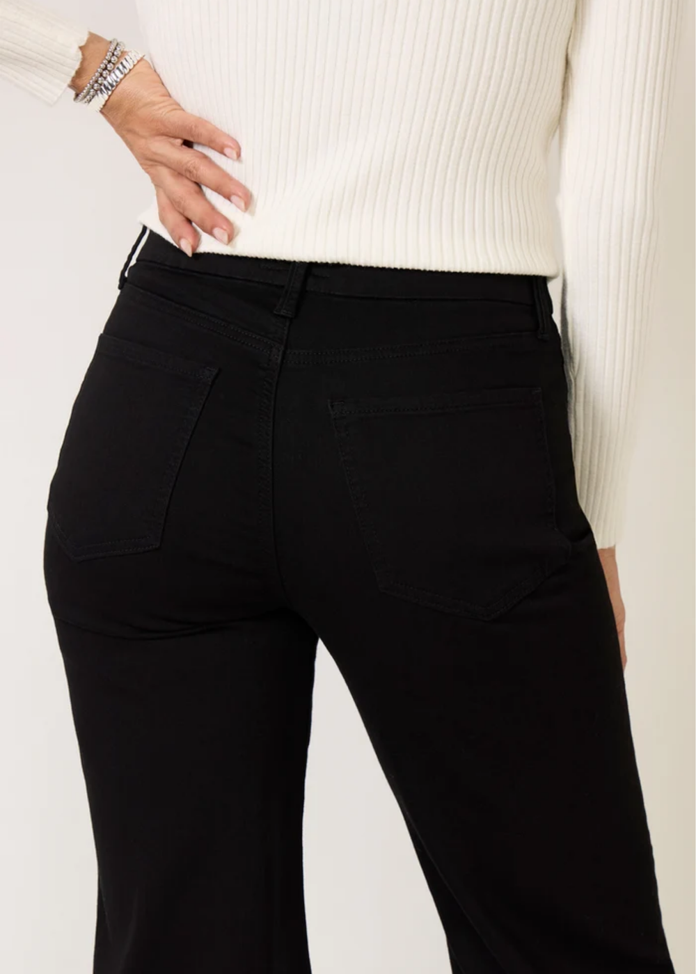 Close-up of a person wearing black high-waisted pants with a ribbed cream sweater, showing the back pockets and waistband.