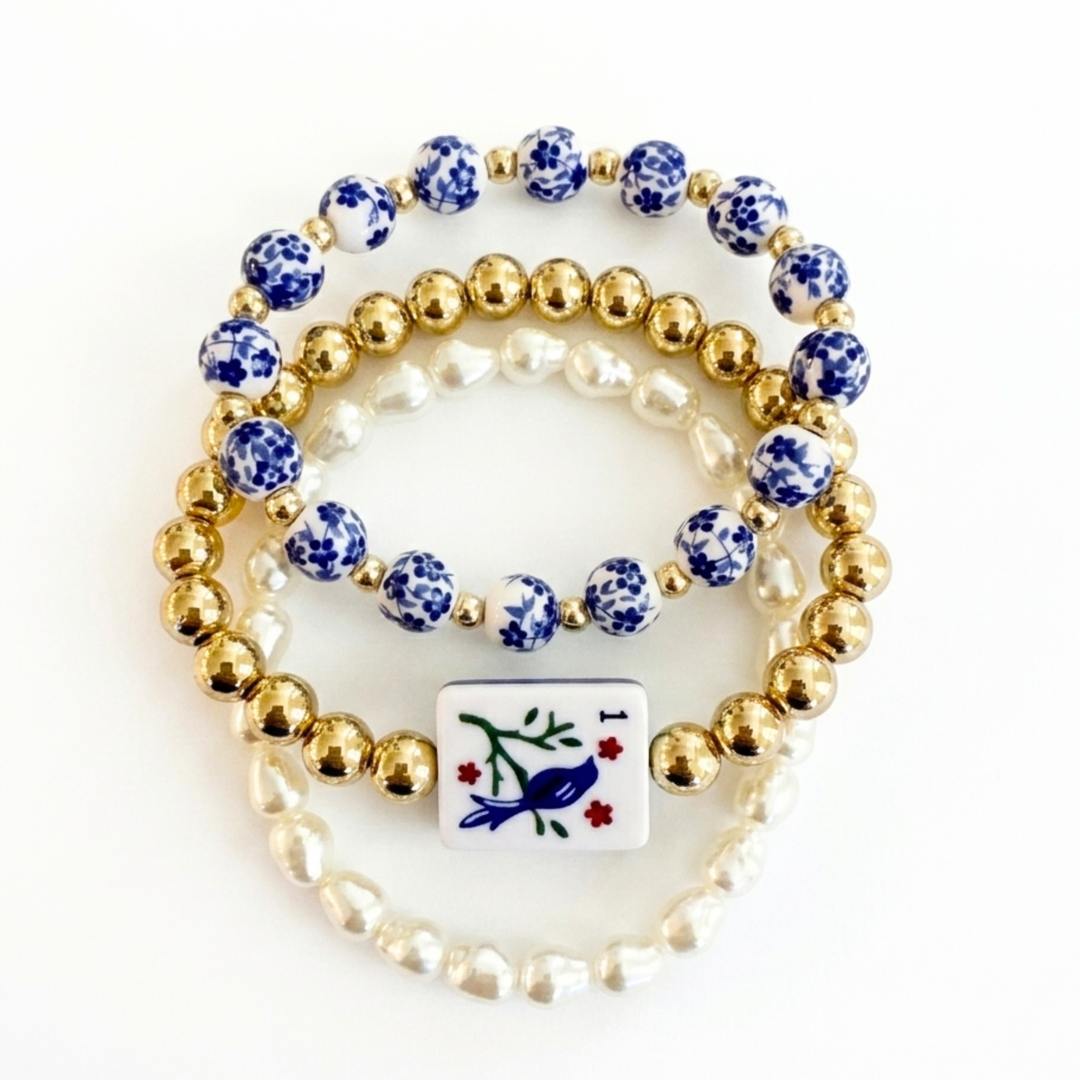 Set of three bracelets with blue and white beads, gold beads, and a decorative tile charm on a white background.