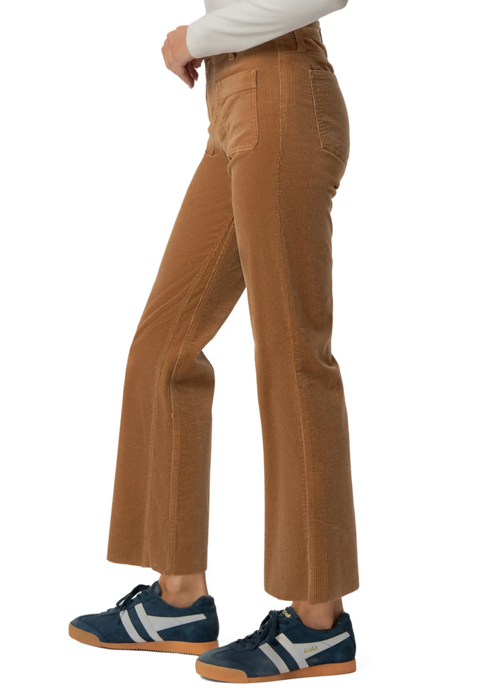 A person shown from the waist down wearing tan corduroy flared pants and navy sneakers with white stripes, against a plain white background.