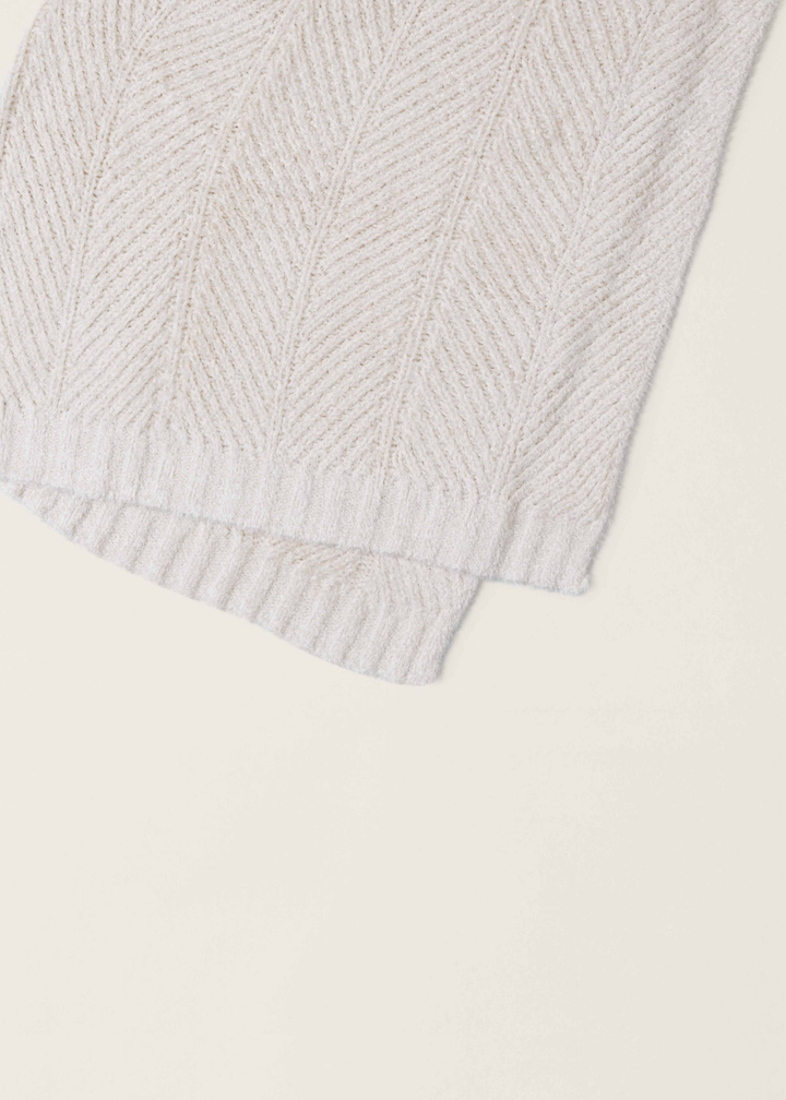 Close up of a cream colored herringbone pattern blanket folded over and laying on a white background