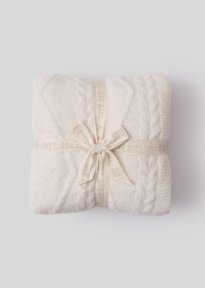 Folded cream blanket tied together with a cream ribbon sitting on a white background