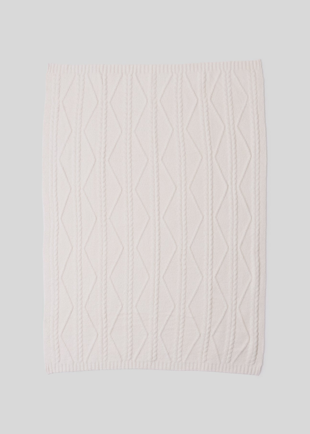 A cream blanket with a woven pattern laying on a white background