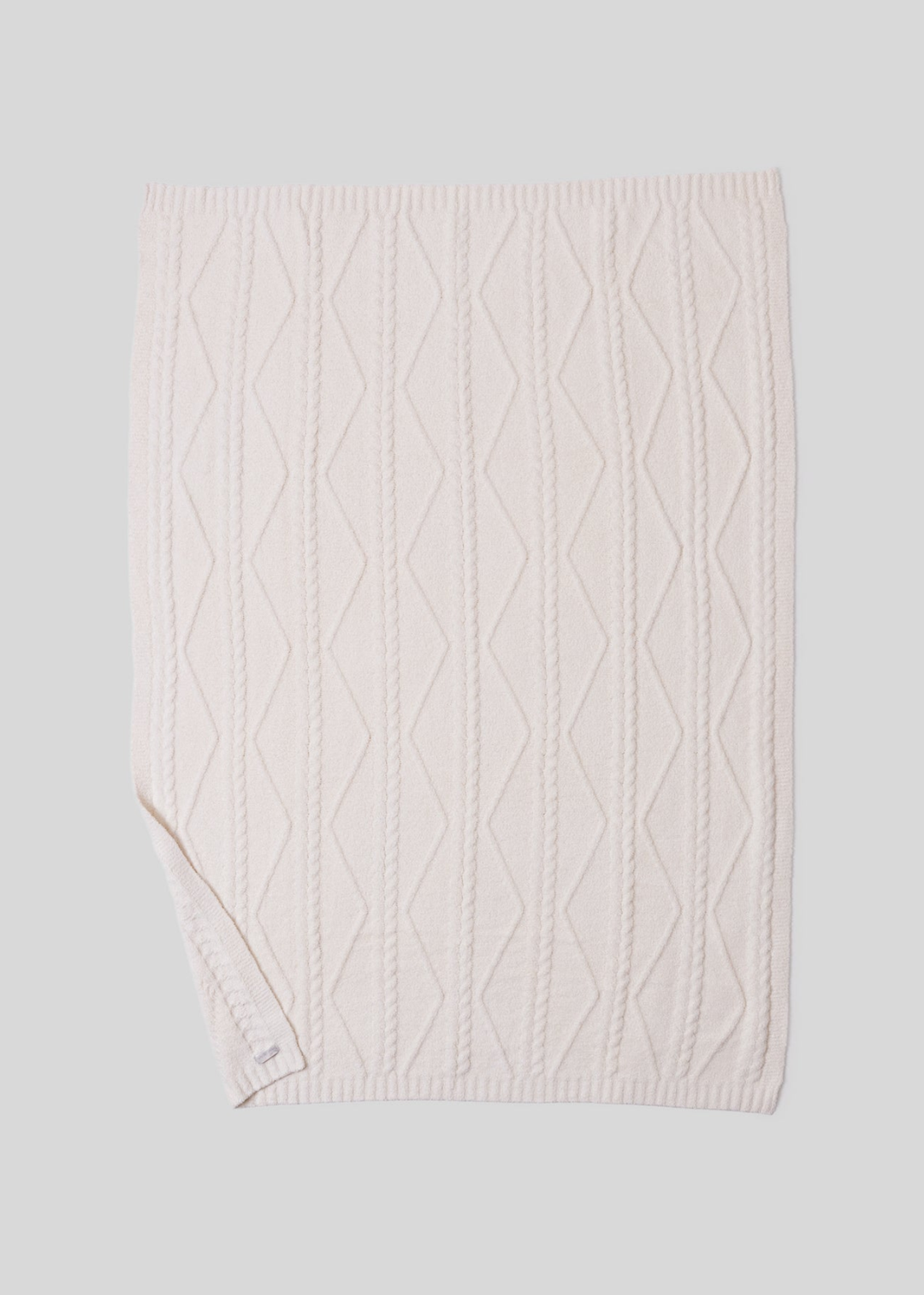 A cream blanket with a woven pattern with a bottom corner folded laying on a white background