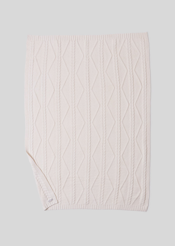 A cream blanket with a woven pattern with a bottom corner folded laying on a white background