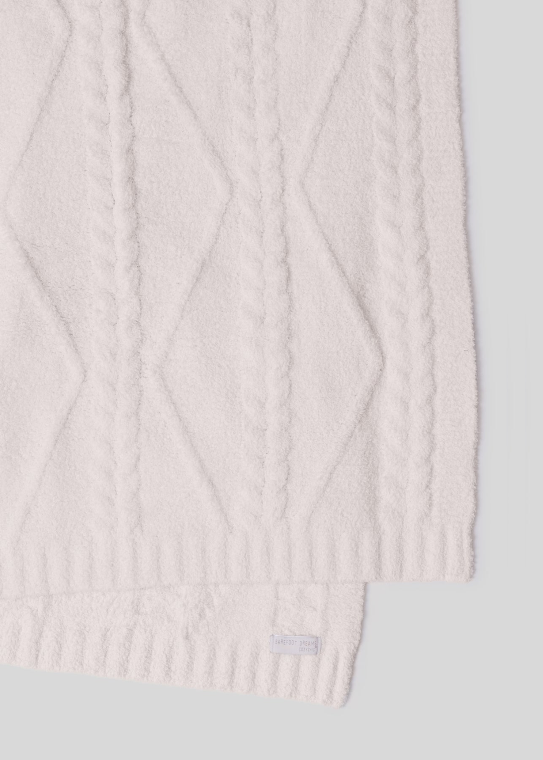 A cream blanket with a woven pattern laying on a white background
