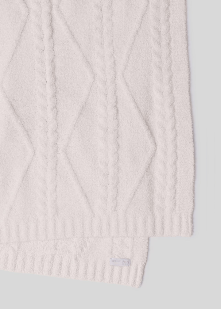 A cream blanket with a woven pattern laying on a white background