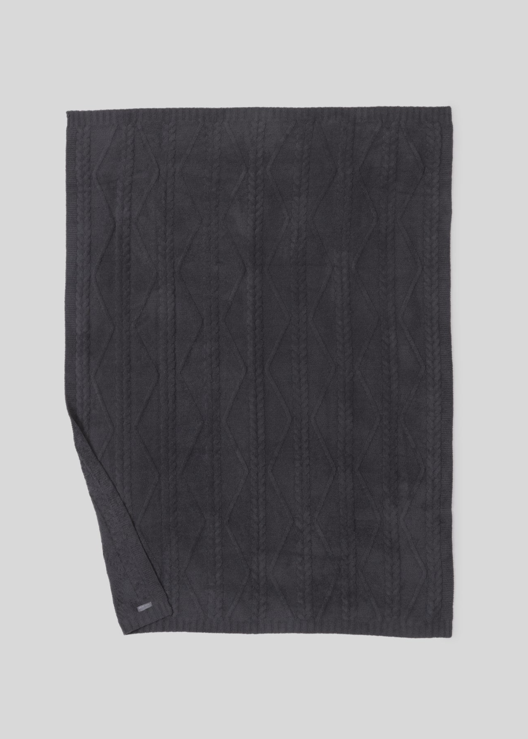 Dark grey blanket with a woven pattern with the bottom corner folded laying on a white background