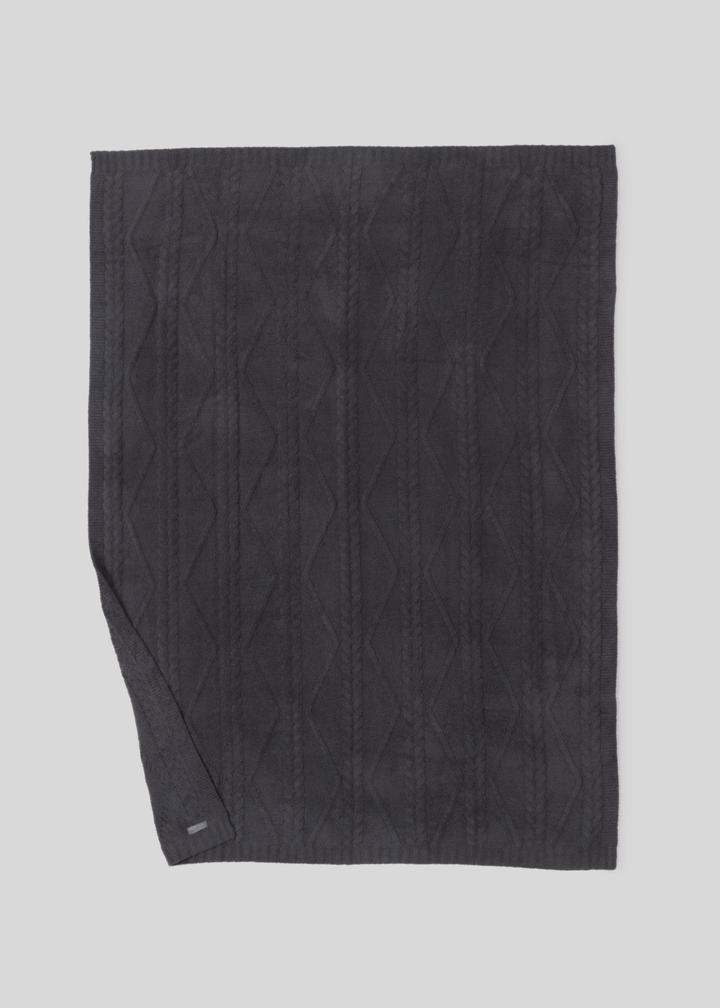 Dark grey blanket with a woven pattern with the bottom corner folded laying on a white background