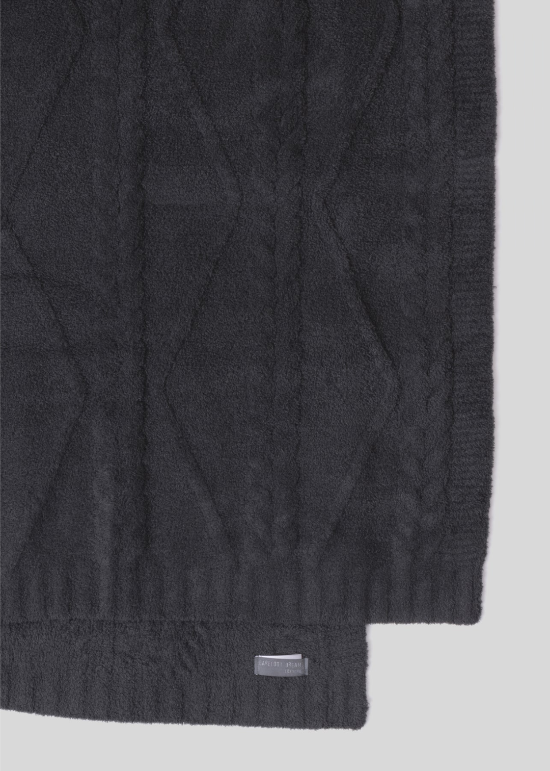Dark grey blanket with a woven pattern with folded over laying on a white background