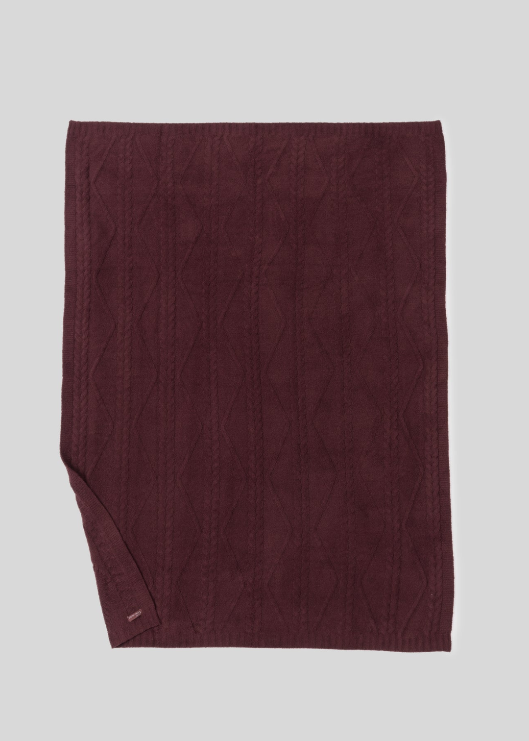 Maroon blanket with a woven pattern and the bottom corner folded up laying on a white background