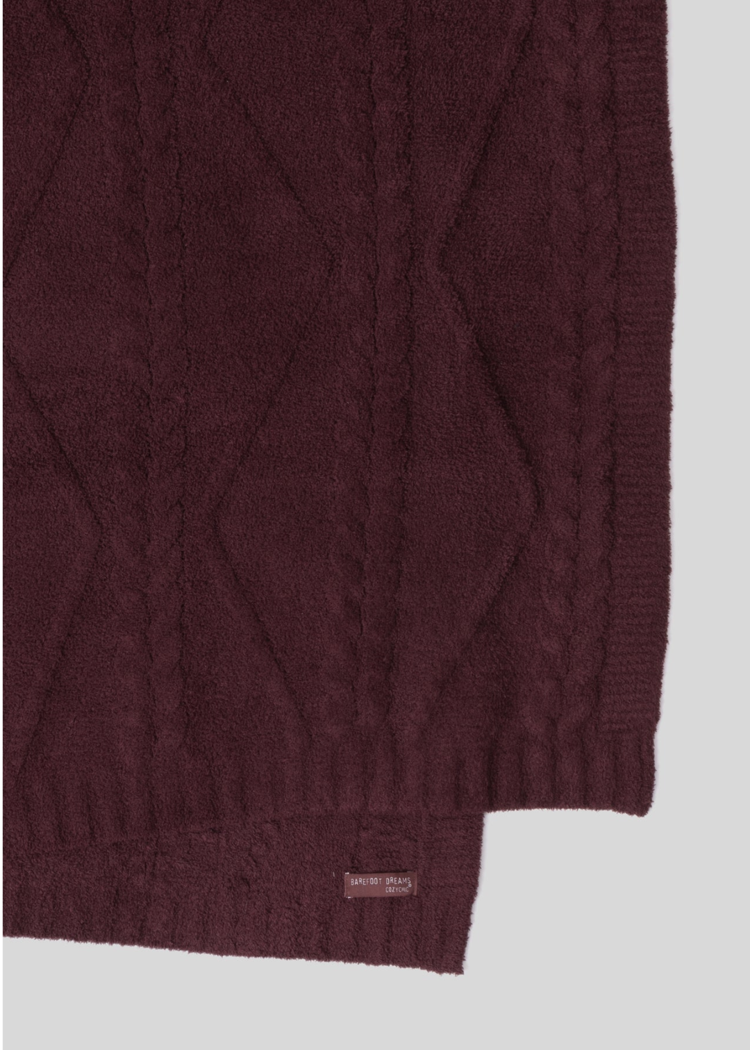 Close up of a maroon blanket with a woven pattern folder over laying on a white background