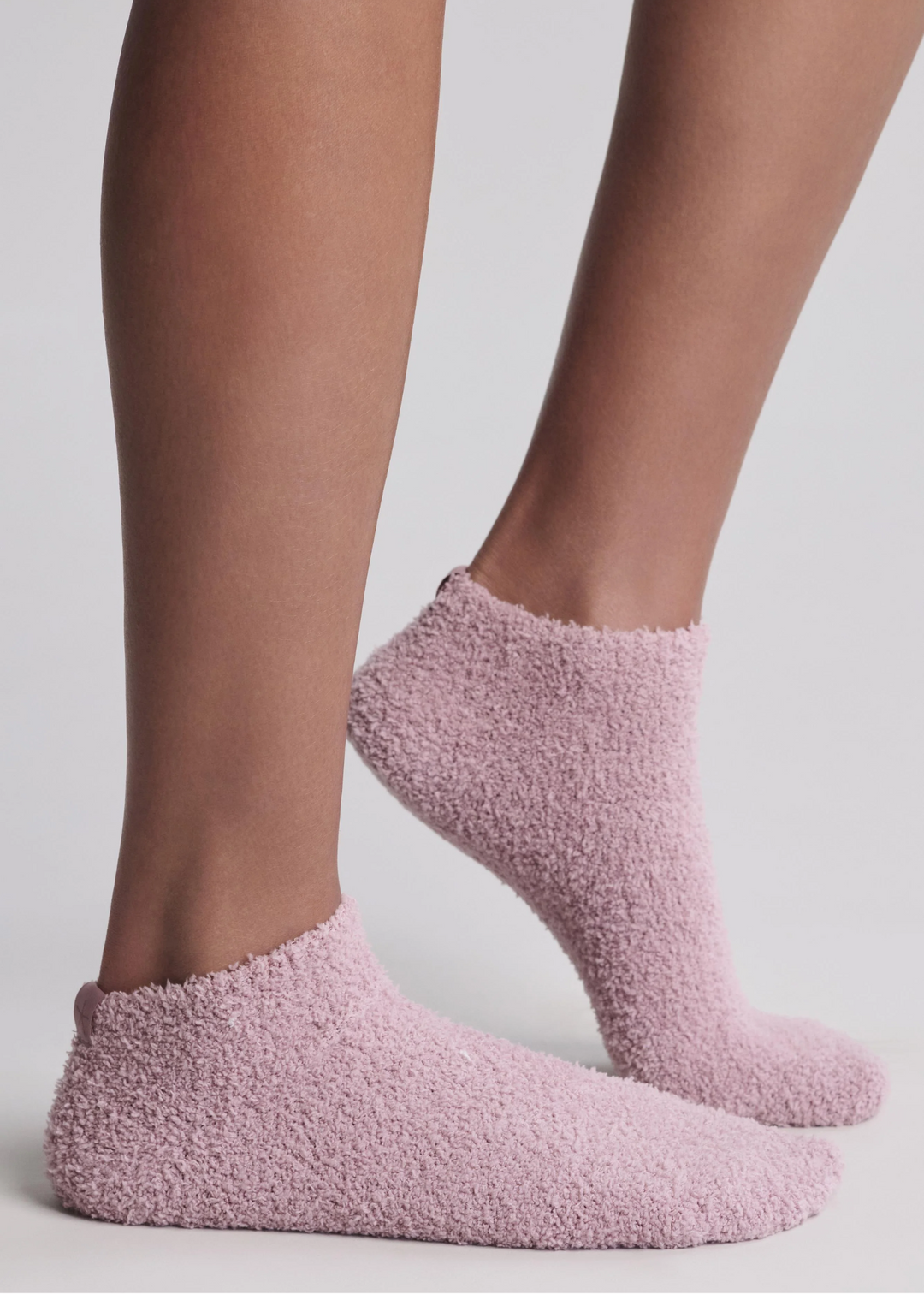 A close up of someone wearing pink ankle socks standing in front of a white background