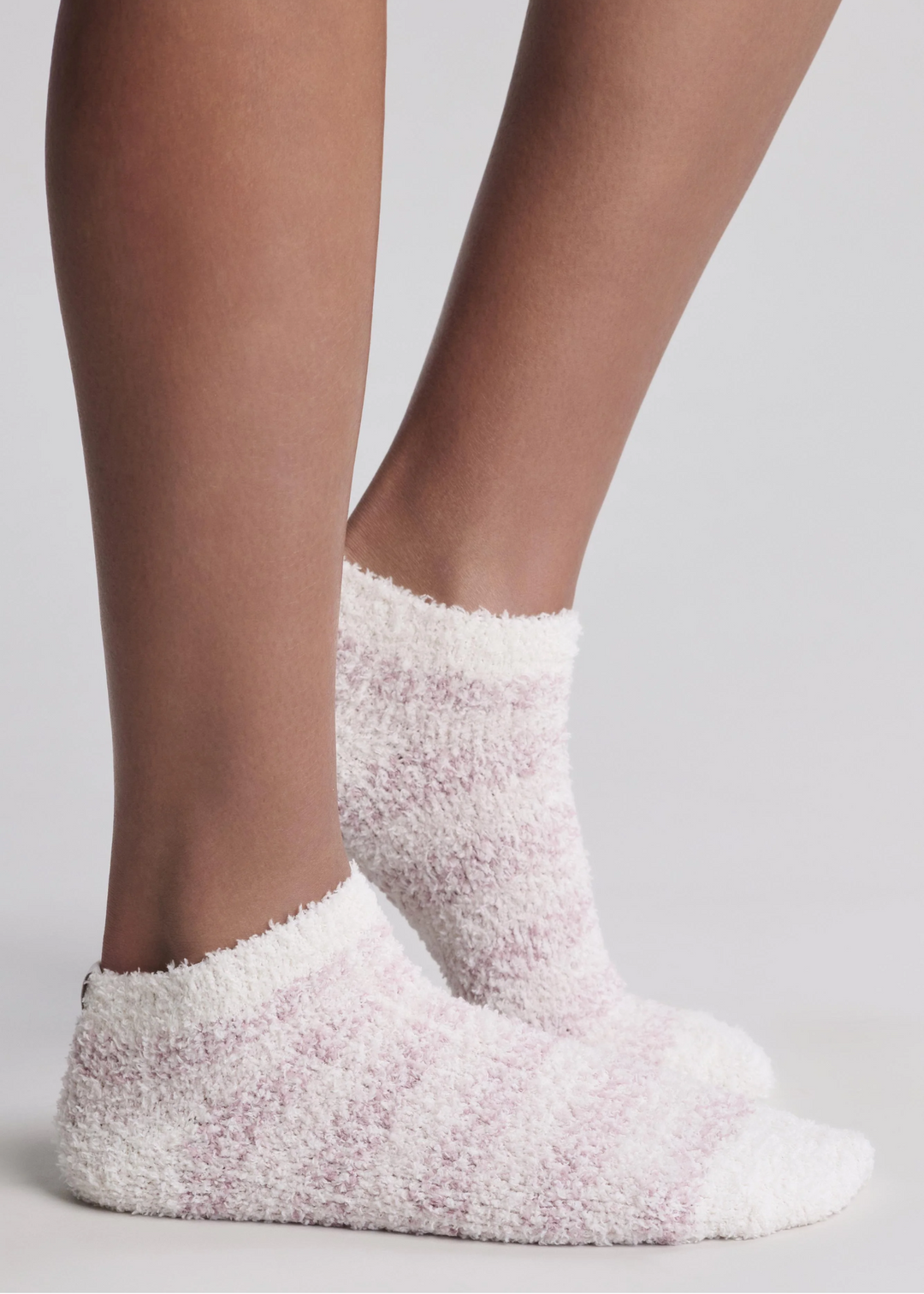 A close up of someone wearing pink and white stripe socks standing in front of a white background