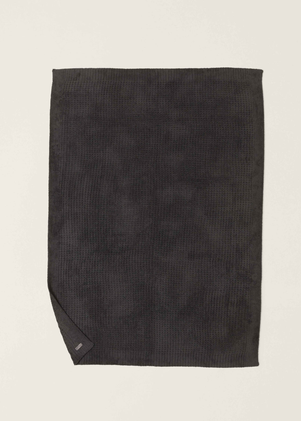 Dark grey waffle knit blanket with a corner folded laying on a white background