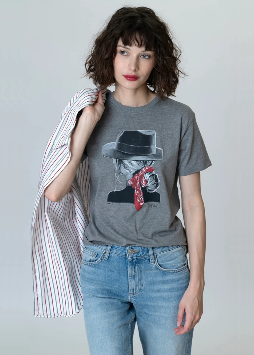 Woman wearing a grey graphic tee with jeans against a grey background