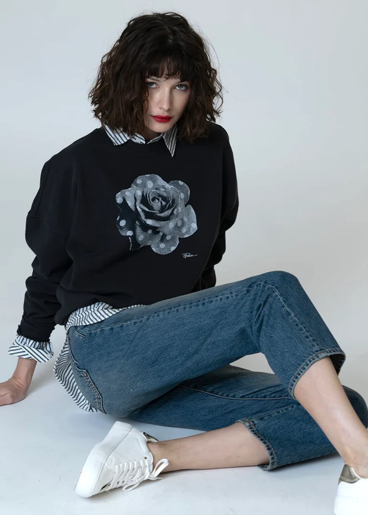 Woman wearing a black sweatshirt with a black and white polka dot rose graphic over a black and white striped button down