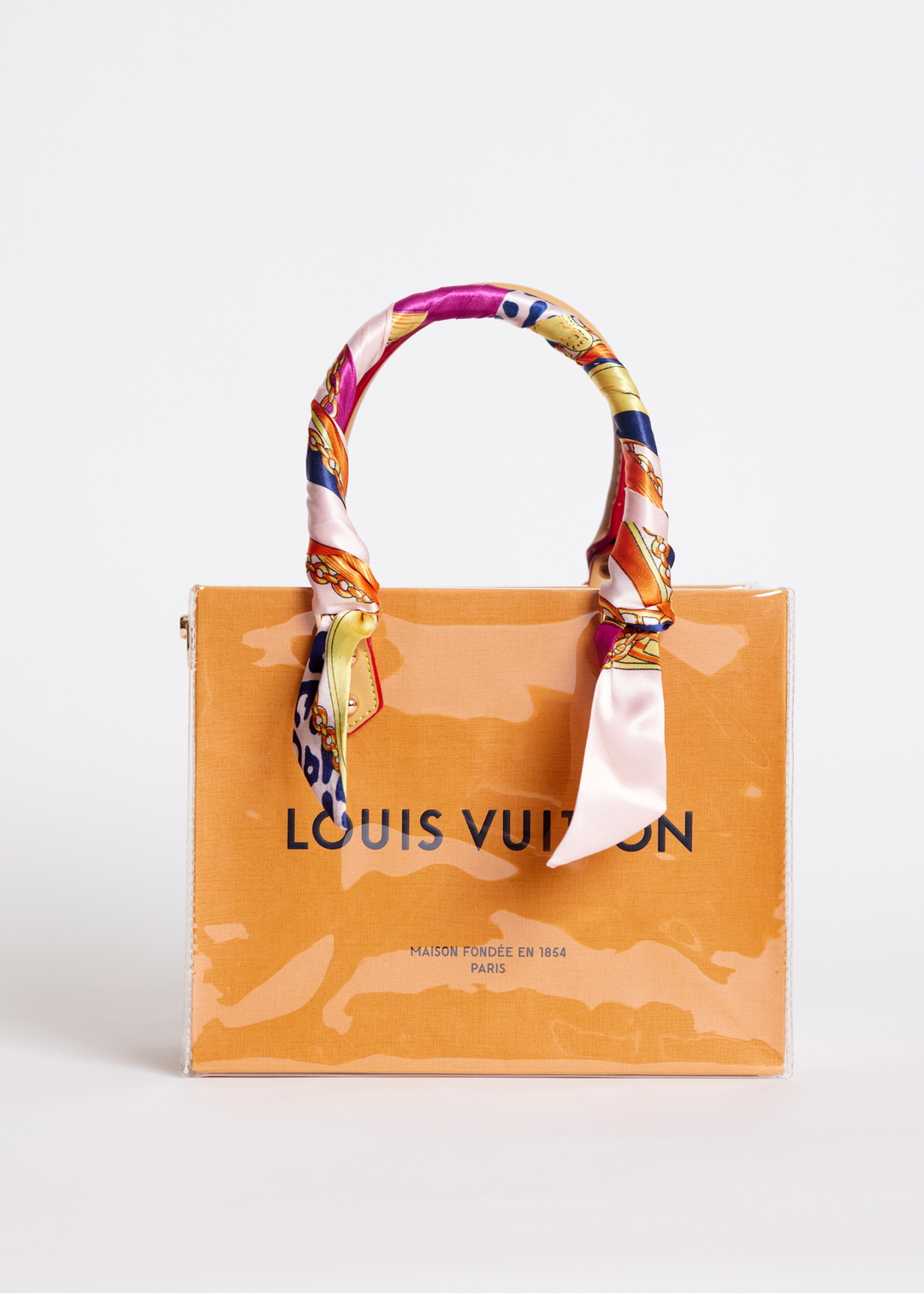 Small clear coated Louis Vuitton shopping bag with a multicolor scarf handle against a white background