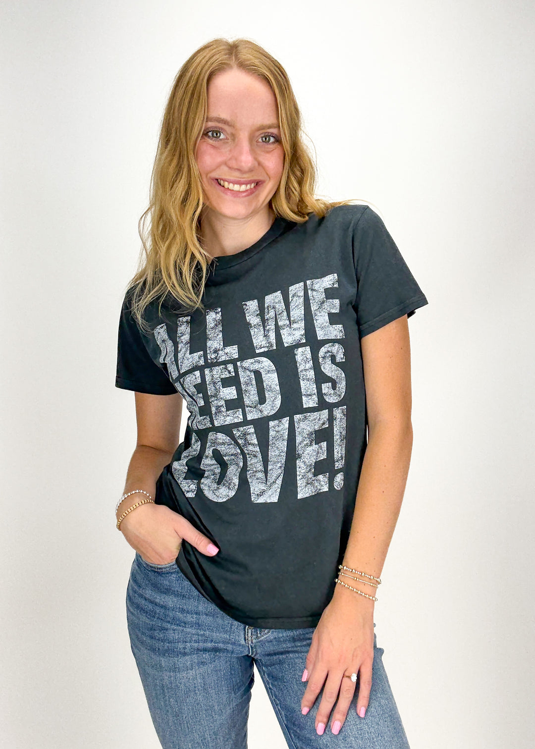 Woman wearing washed black tee with "All We Need Is Love" block letter faded chest graphic