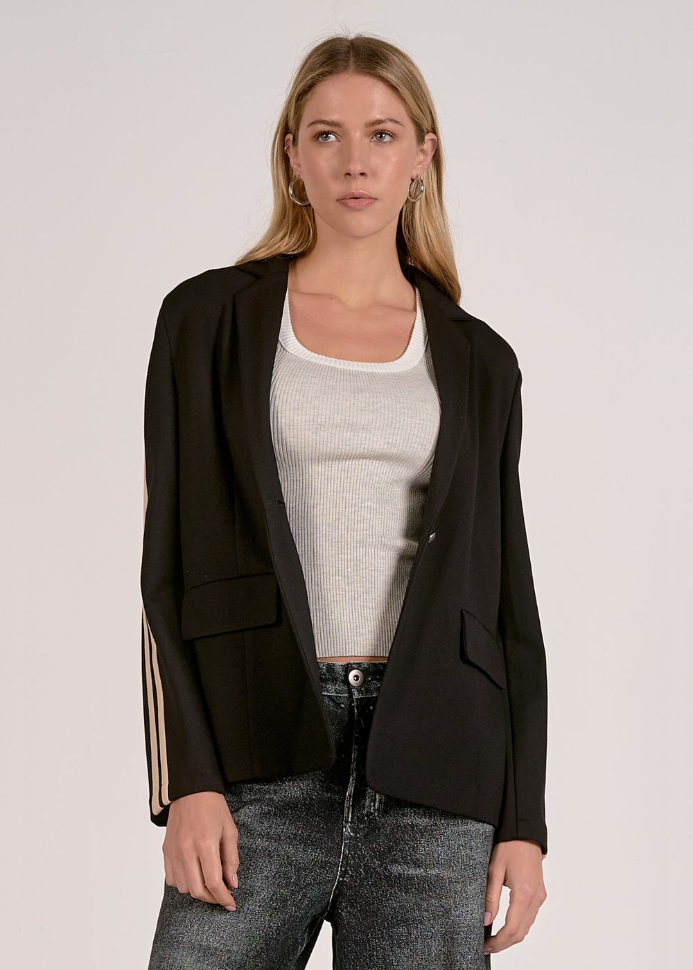 Woman wearing a black blazer with tan sleeve stripes with black washed jeans 