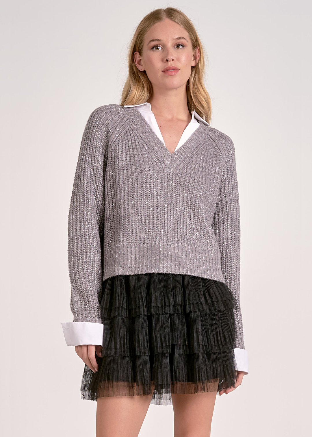 Woman wearing a grey sparkly sweater layered over a white button down with a black mesh skirt