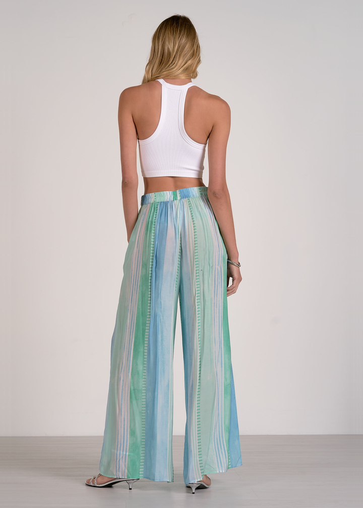 Woman turned around wearing green, blue, and white striped pants with a white crop top and silver heels