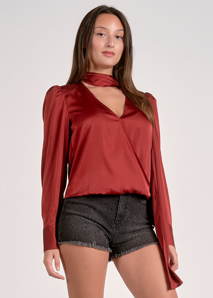 Woman wearing a rust colored top with a v-neck and scarf