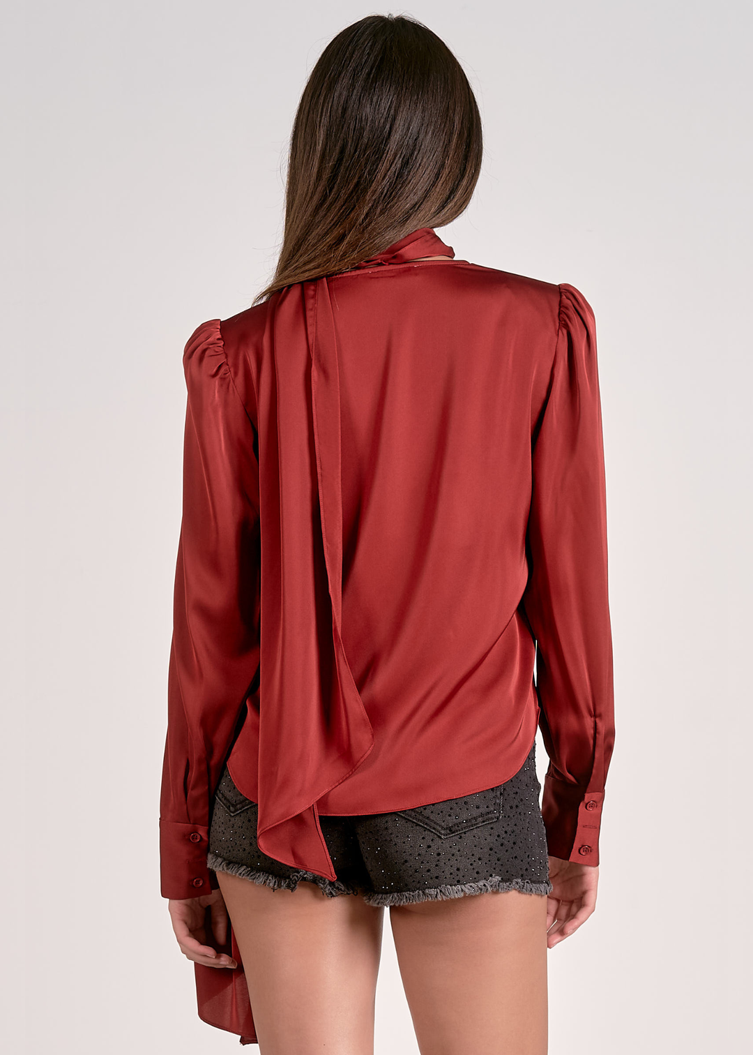 Woman turned around wearing a rust colored top with a v-neck and scarf