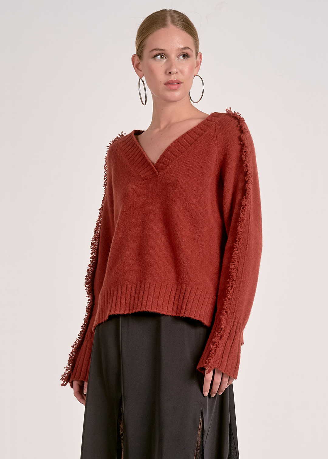 Woman wearing a v-neck rust colored sweater against a white background