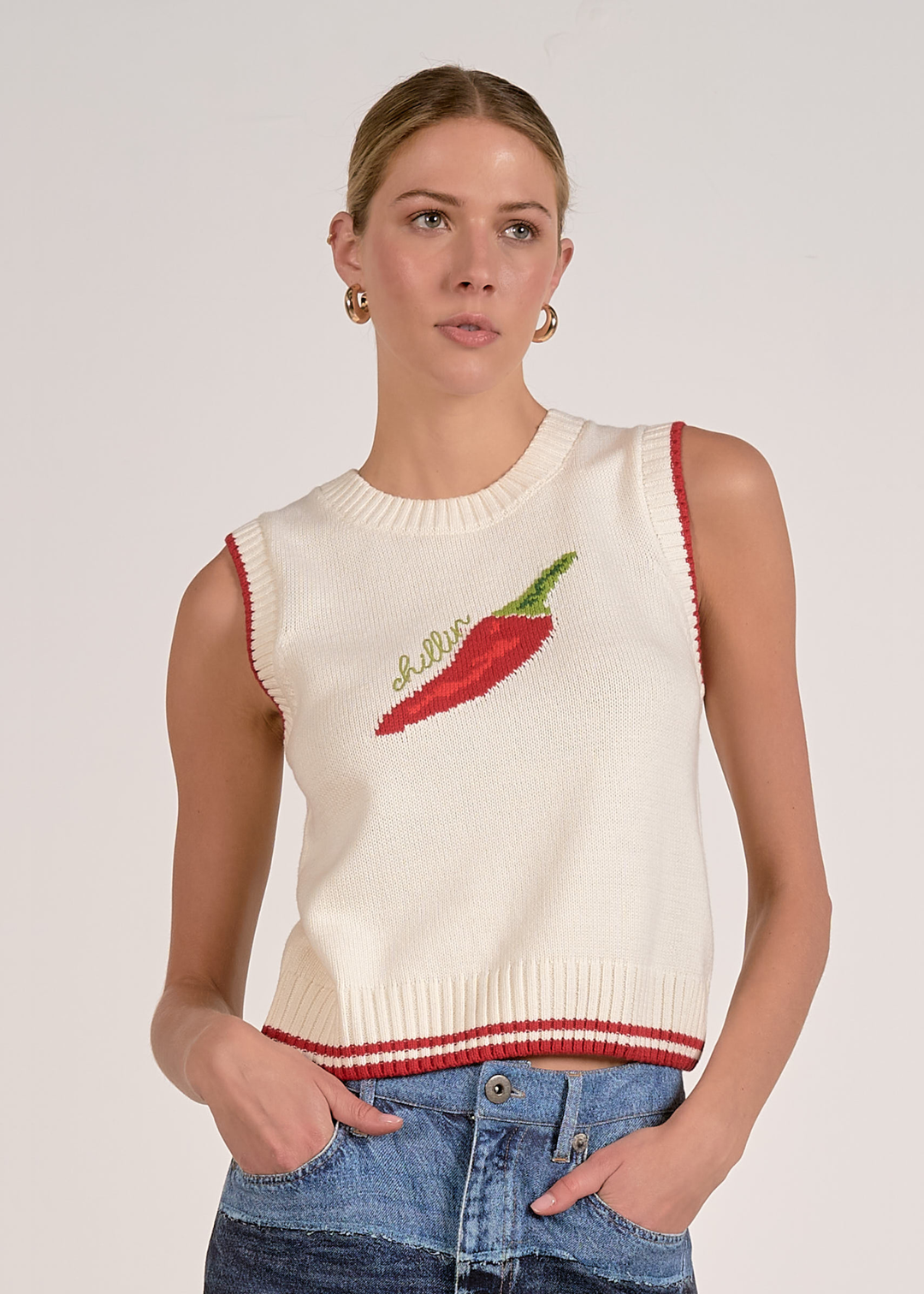 Woman wearing a white sleeveless knit top with a red pepper and "chillin" graphic and jeans