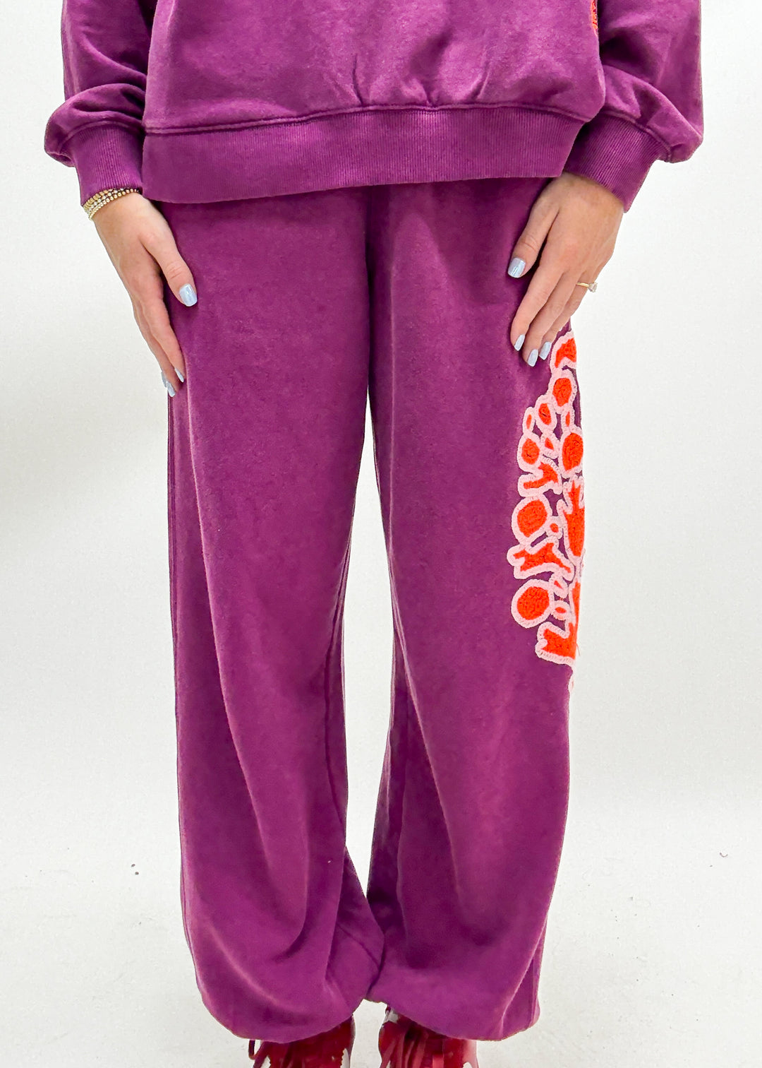 Women's purple jogger sweatpants with orange embroidered FP movement logo on leg