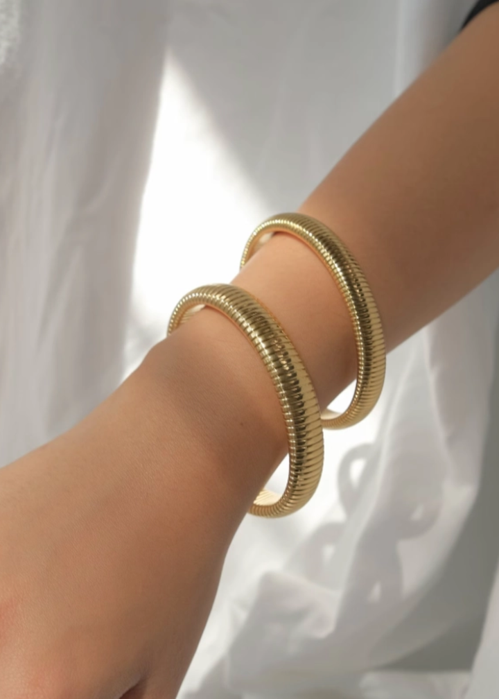 Woman wearing two gold bangle bracelets against a white background