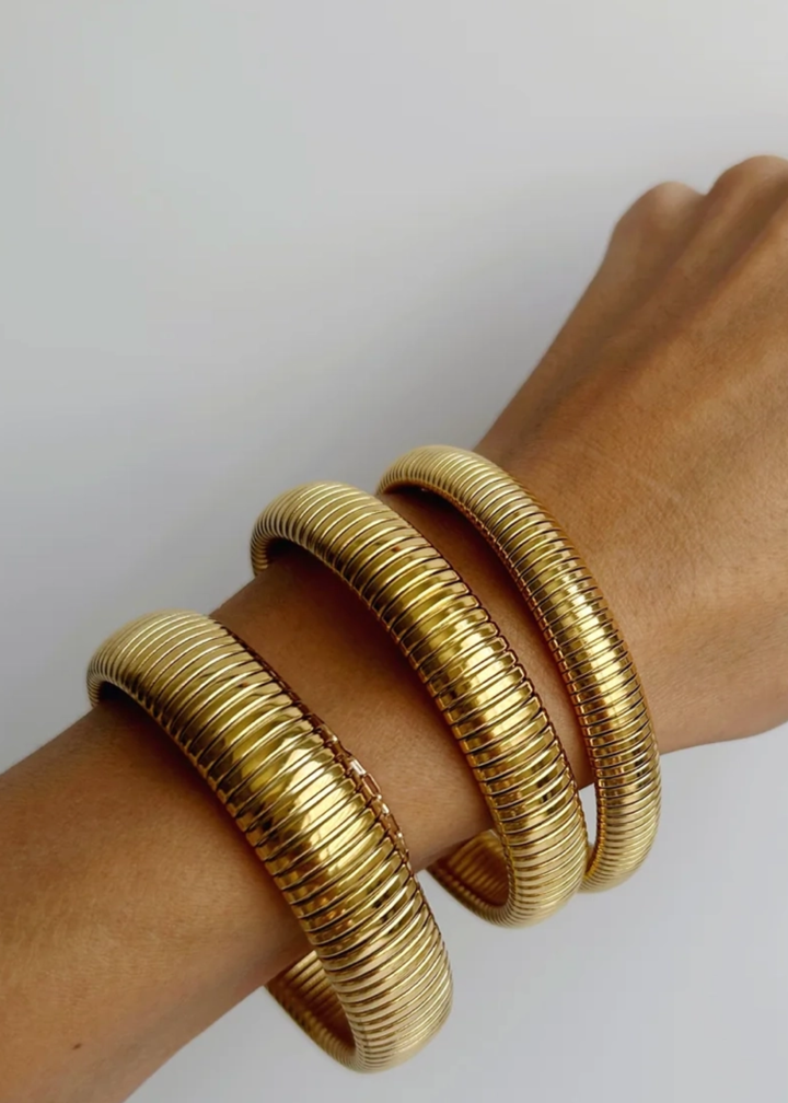 Woman wearing three gold bangle bracelets against a white background