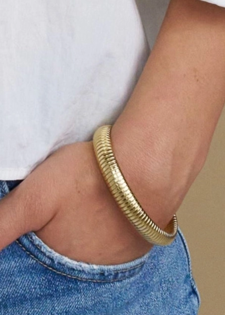 Woman wearing a gold bangle bracelet against a white background