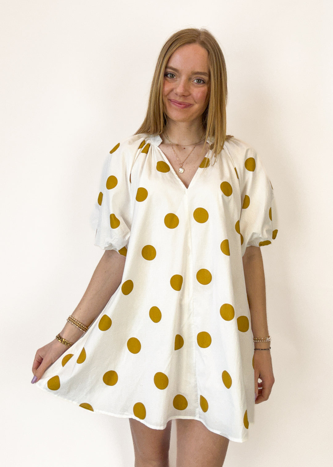 Woman wearing a white dress with gold polka dots against a plain background