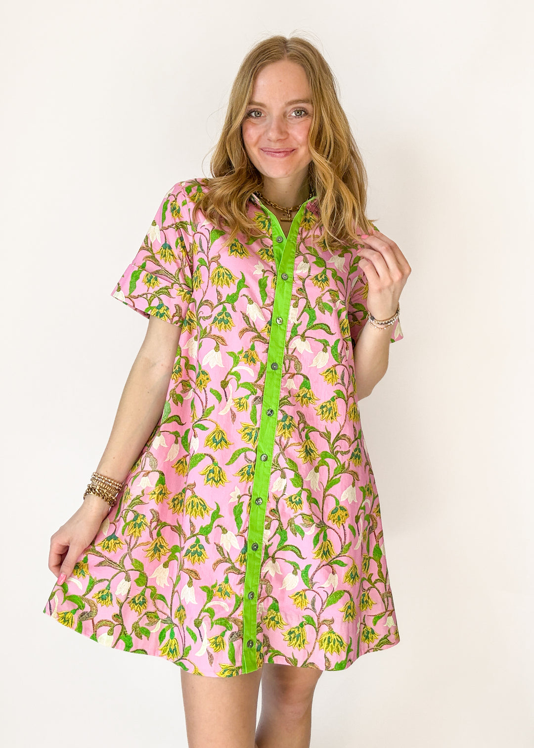 Woman wearing a pink floral dress with green buttons on a white background