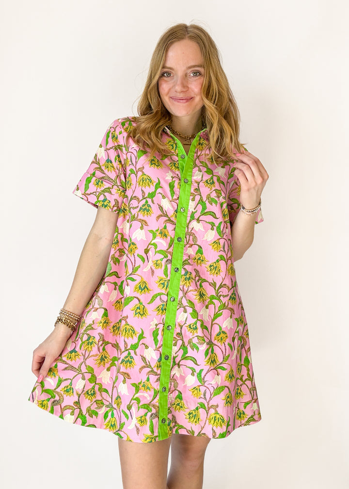 Woman wearing a pink floral dress with green buttons on a white background