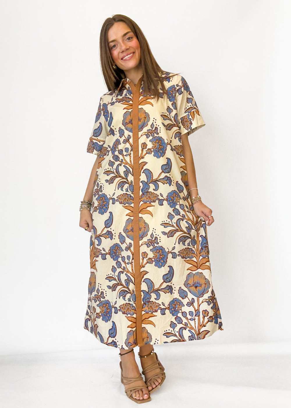 A woman modeling a short-sleeved midi dress with a cream base and a brown and blue floral block print, standing against a plain white studio background.
