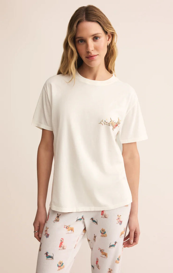 Woman wearing a white t-shirt with a small logo and patterned pants on a beige background