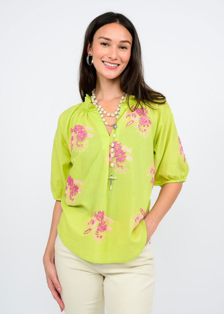 A woman wearing a celery green top with a pink floral pattern in front of a white background
