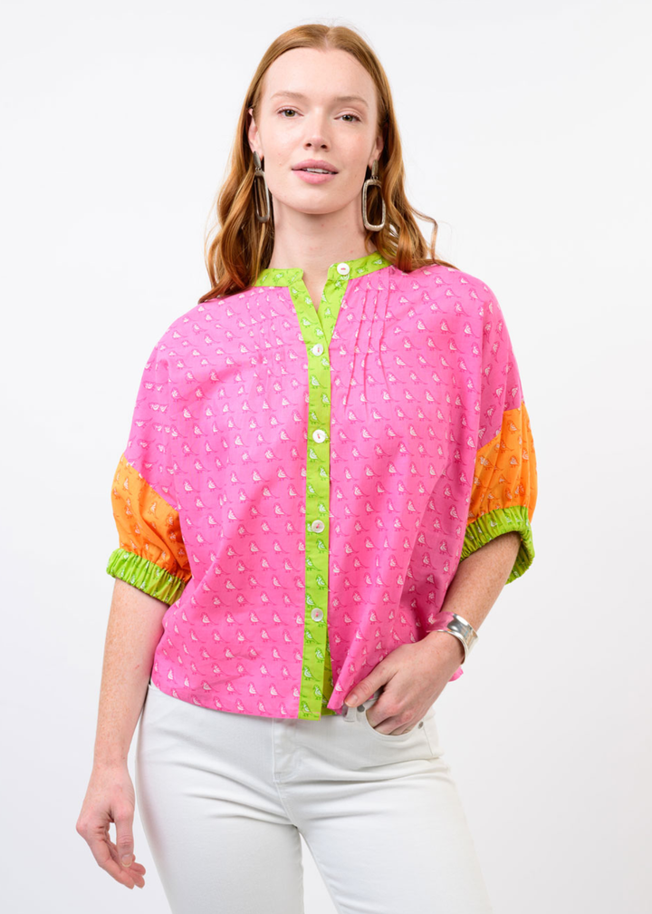 Woman wearing a pink top with a small bird pattern and orange half sleeves and green trim