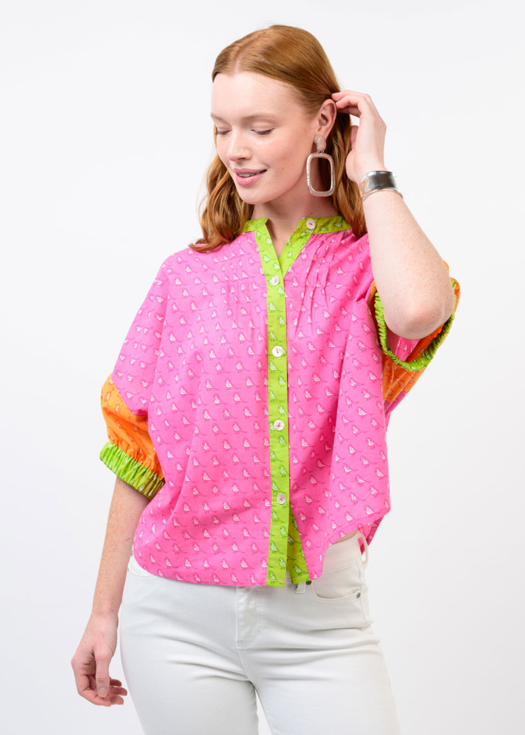 Woman wearing a pink top with a small bird pattern and orange half sleeves and green trim