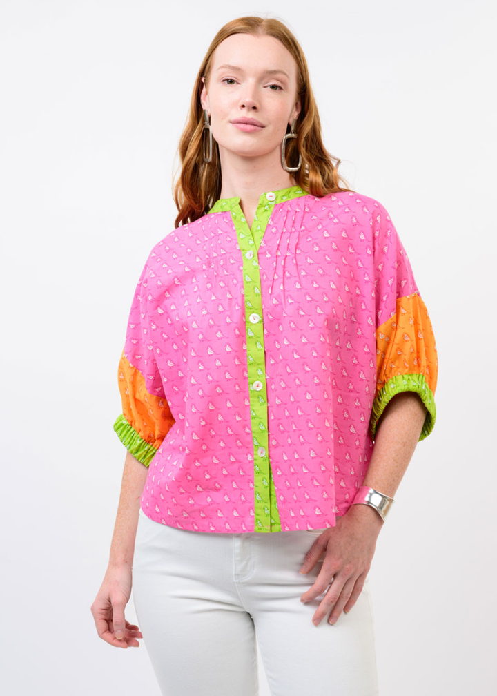 Woman wearing a pink top with a small bird pattern and orange half sleeves and green trim
