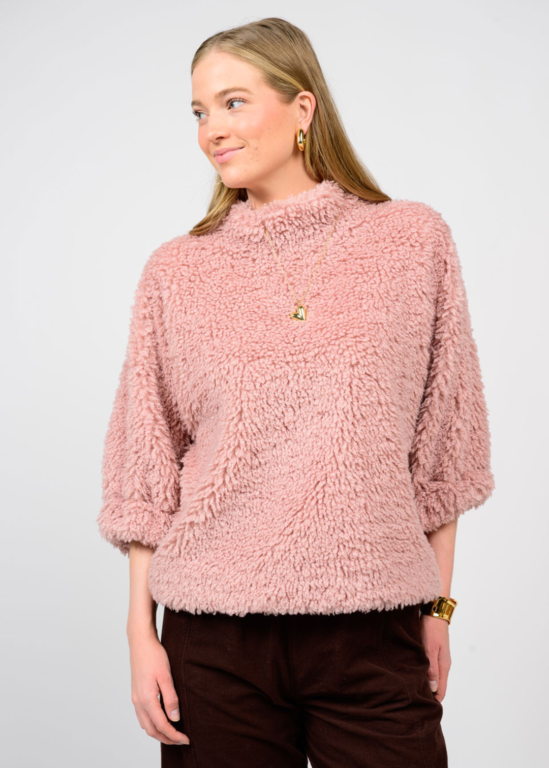 Woman wearing a pink sherpa top with 3/4 length sleeves and black jeans in front of a white background