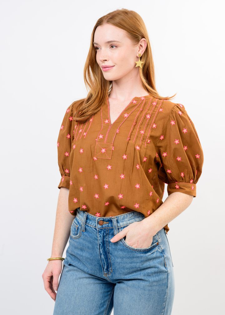 Woman wearing a rust colored top with a pink pattern and jeans