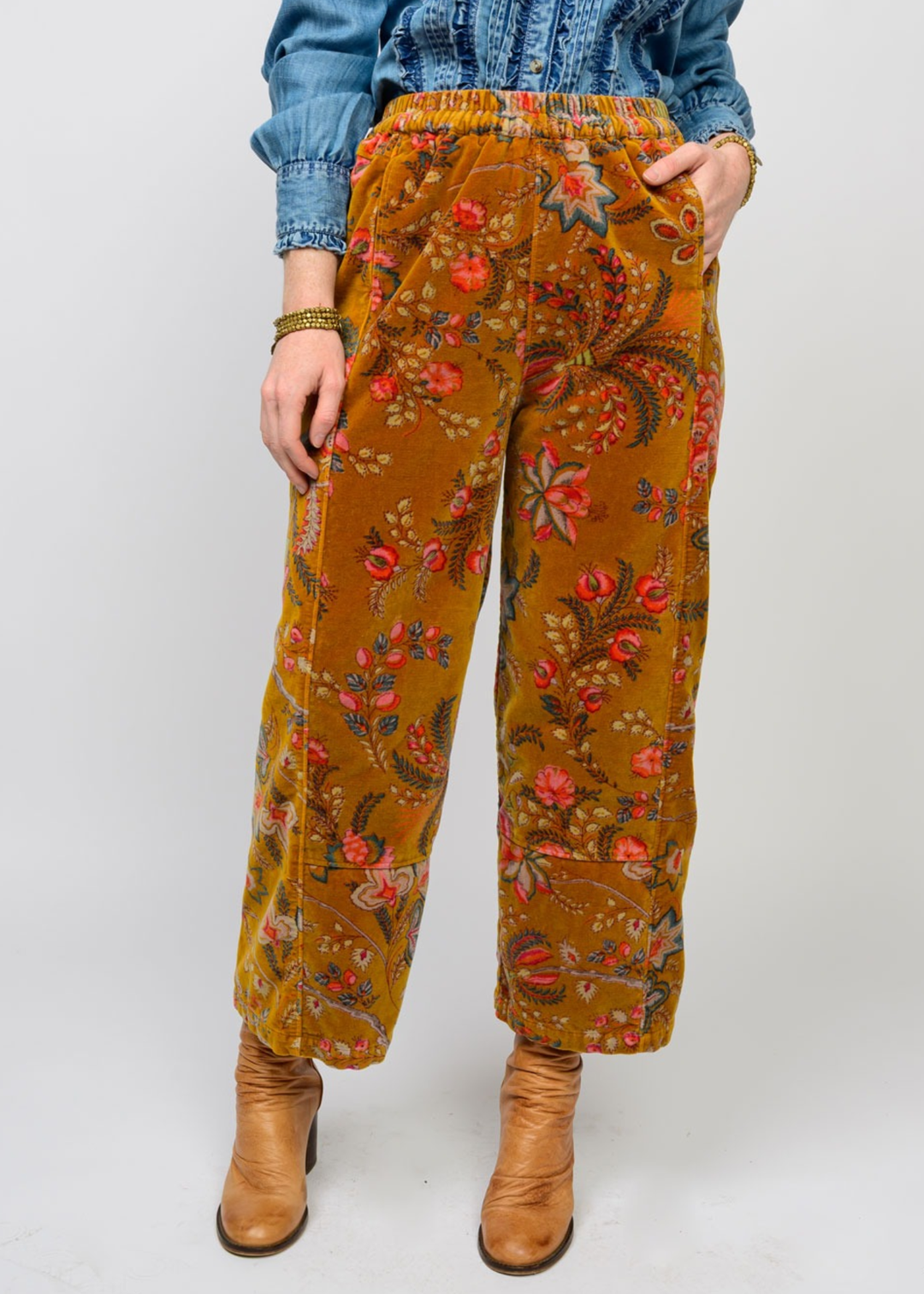 Woman wearing gold barrel pants with a floral print and brown boots in front of a white background