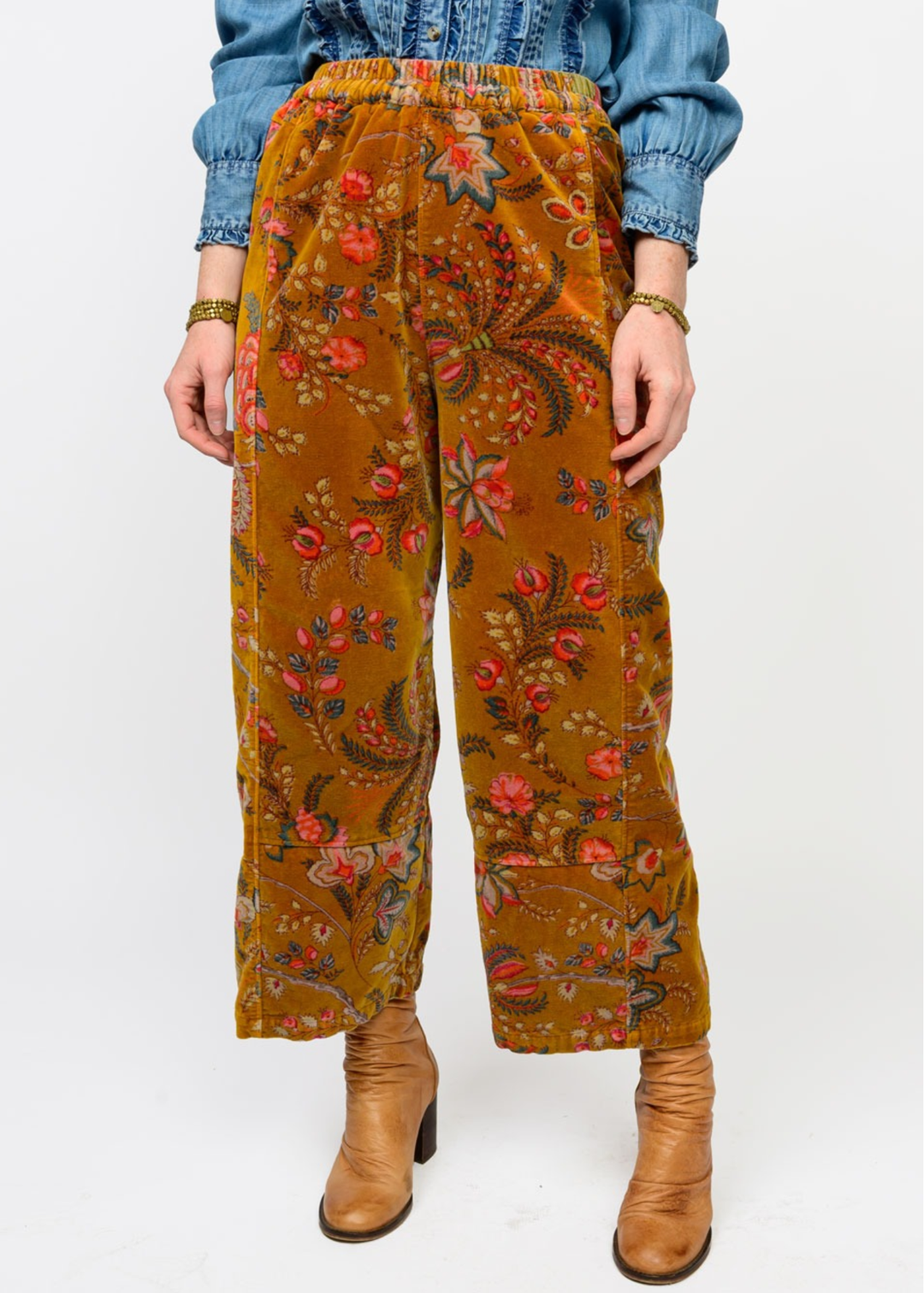 Woman wearing gold barrel pants with a floral print and brown boots in front of a white background