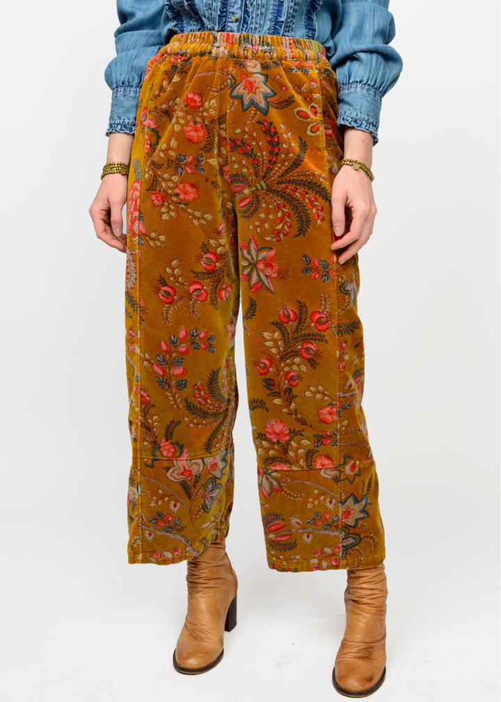 Woman wearing gold barrel pants with a floral print and brown boots in front of a white background