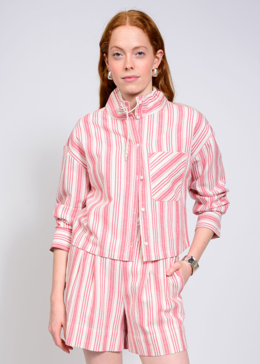 Woman wearing a mock neck and 3/4 length sleeve pink and white striped top with matching shorts