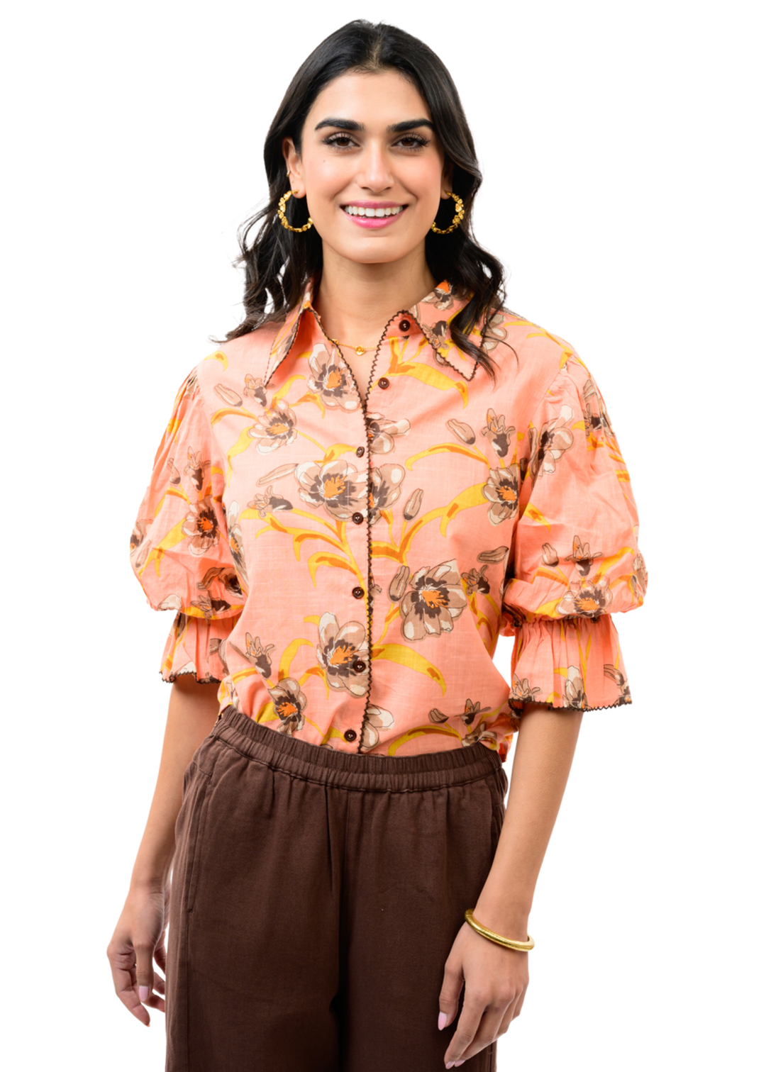 Woman wearing a coral floral button down top with puff sleeves and brown pants